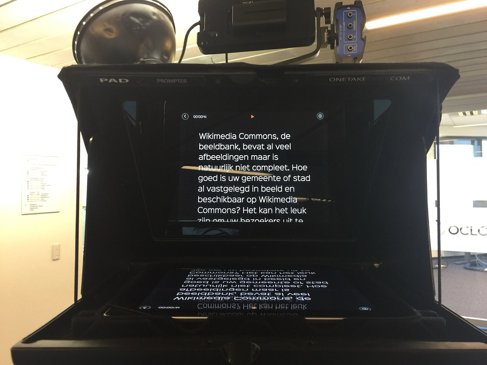 A tablet teleprompter: the script on a screen below is reflected, mirrored, in angled glass above