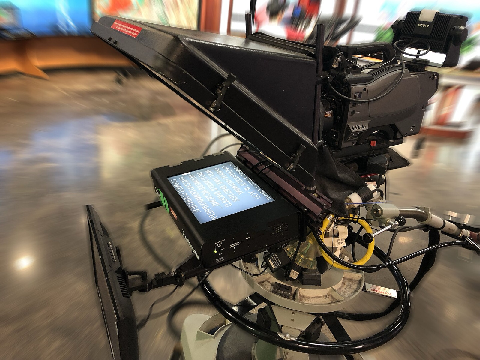 A studio camera fitted with a teleprompter hood and a script monitor